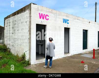 Porto Moniz Madeira Portugal. A woman waits outside the female toilet of a car park toilet block. Stock Photo