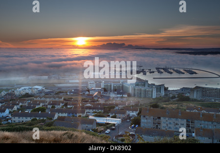 View from Portland looking over the marina and harbour towards Chesil Beach with incoming sea mist at sunset Stock Photo