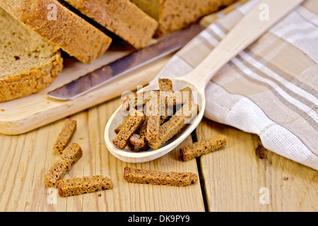 Rye homemade bread, croutons in a wooden spoon, knife, napkin on the background of wooden boards Stock Photo
