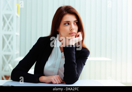 Young thoughtful businesswoman sitting on her workplace and looking away in office Stock Photo