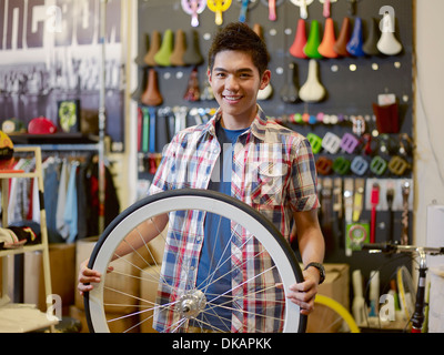 Portrait of young man in bike shop holding bicycle wheel Stock Photo