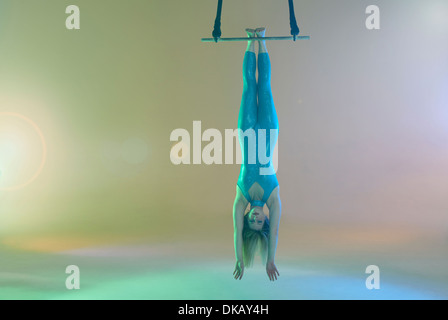 Trapeze artist hanging upside down on trapeze Stock Photo