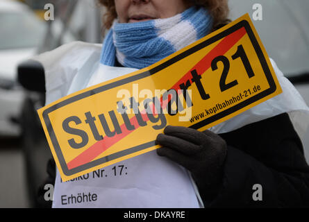 Stuttgart, Germany. 04th Dec, 2013. An opponent to the controversial railway project Stuttgart 21 holds a sticker near a tunnel contruction pit in Stuttgart, Germany, 04 December 2013. It is the first dig on the first tunnel of Stuttgart 21. Photo: MARIJAN MURAT/dpa/Alamy Live News Stock Photo