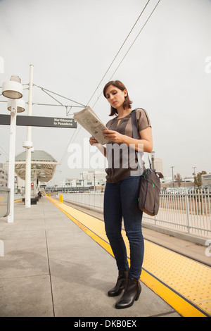 Woman reading newspaper whilst waiting at station, Los Angeles, California, USA Stock Photo