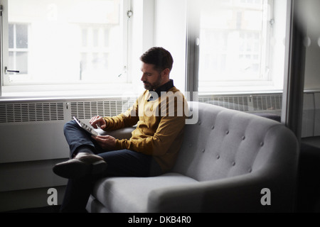 Casual businessman sitting on sofa using digital tablet Stock Photo