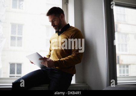 Casual businessman sitting on windowsill using digital tablet Stock Photo