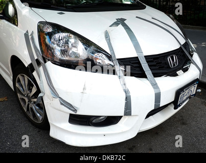 The front end of a white parked car held together with silver duct tape. Stock Photo