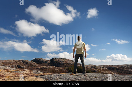 Young man staring at blue sky stands on rocky ground