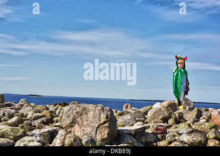 Boy wearing green cape standing on stone wall, Eggergrund, Sweden Stock Photo