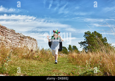 Boy wearing green cape running along grass, Eggergrund, Sweden Stock Photo