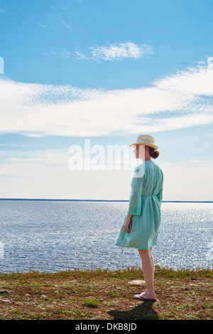 Mid adult woman standing by sea in green dress, Eggergrund, Sweden Stock Photo