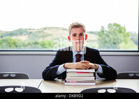 Teenage schoolboy sitting at desk with pile of books Stock Photo
