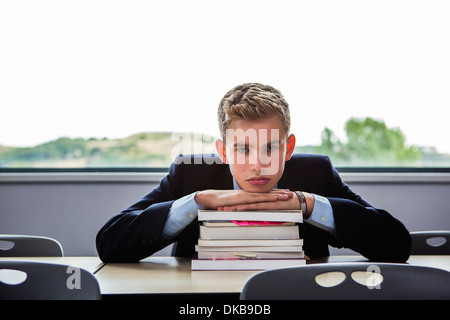 Teenage schoolboy sitting at desk with head on pile of books Stock Photo