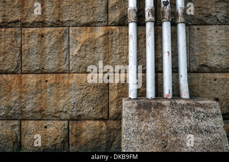 Pipes embedded in a concrete block against a stone wall. Stock Photo