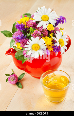 red teapot with bouquet of healing herbs and flowers, cup of healthy tea on table, herbal medicine Stock Photo