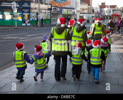 K ids walking across street in Blackpool, Lancashire, UK 4th December, 2013.   Rear view of risk assessed Pre-school children and teachers, safeguarded wearing santa hats & high visibility clothing, en-route to the Winter Gardens Blackpool Opera House Theatre Open day.  An opportunity to access all areas, free of charge, something never done before at the Winter Gardens, to celebrate 135 with the local community and visitors of Blackpool. Stock Photo