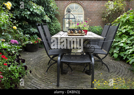 Iron forged table and chairs in garden with flowers, table decoration and potplants in summer Stock Photo