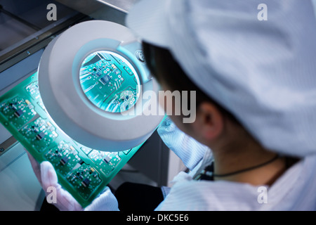 Worker at small parts manufacturing factory in China looking through magnifier at microchips Stock Photo