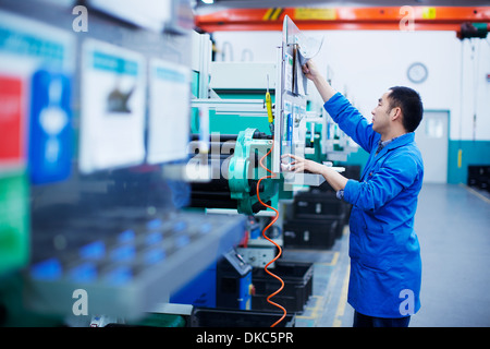 Worker at small parts manufacturing factory in China, reaching up to press button on control panel Stock Photo
