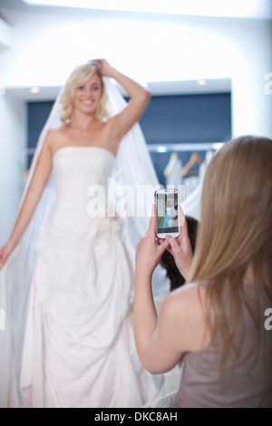 Young woman taking photograph of friend trying on wedding dress Stock Photo