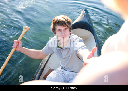 Young man in rowing boat reaching up to female friends Stock Photo