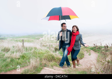 Couple on coast walk carrying umbrella, Thurlestone, Devon, UK Stock Photo