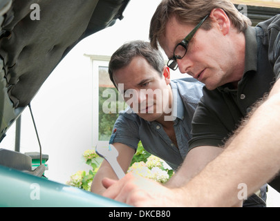 Two male adult friends checking under car hood Stock Photo