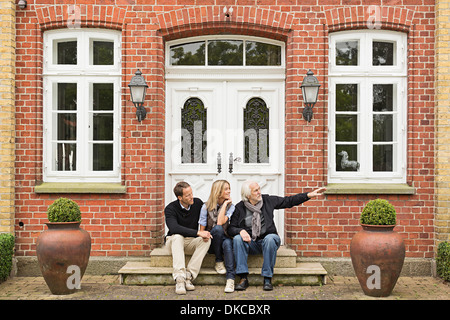 Father and mid adult couple sitting on doorstep Stock Photo