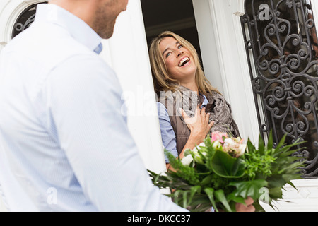 Woman opening front foor, man with bouquet Stock Photo