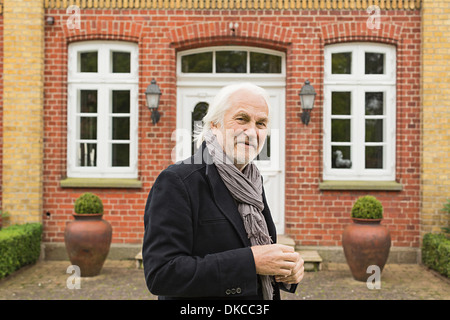 Portrait of senior man wearing jacket and scarf outside house Stock Photo