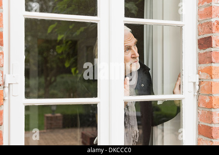 Senior man looking through window Stock Photo