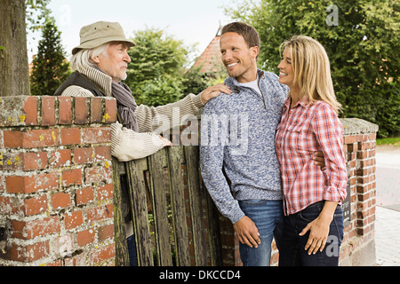 Senior man leaning on gate talking to with mid adult couple Stock Photo