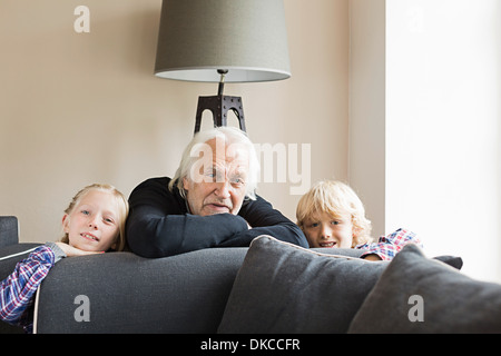 Portrait of grandfather and grandchildren leaning on sofa Stock Photo