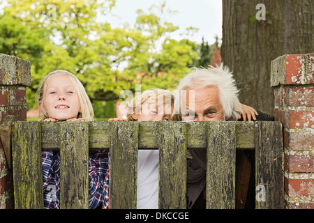 Grandfather and grandchildren peering over wooden gate Stock Photo