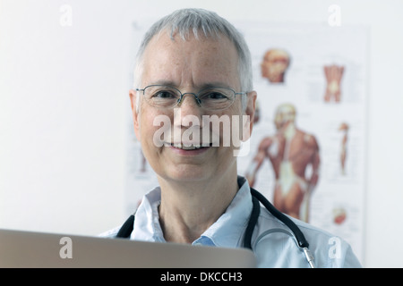 a laughing  woman doc with a human muscle person poster in the background and a laptop Stock Photo