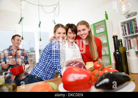 Portrait of mother with daughters in kitchen, son in background Stock Photo