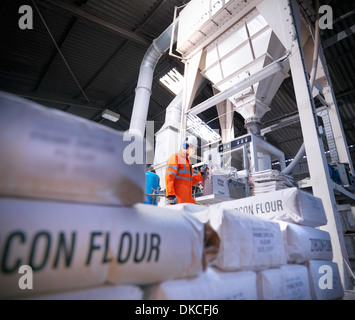 Worker in protective clothing filling zircon flour bags in mill, low angle view