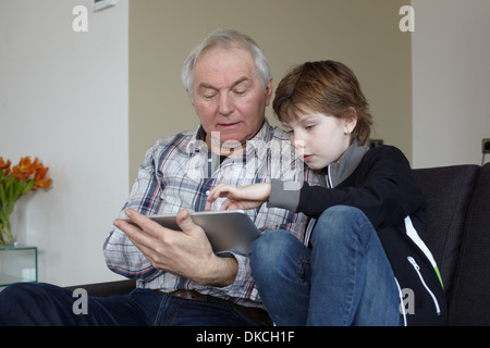 Senior man with grandson at home using digital tablet Stock Photo