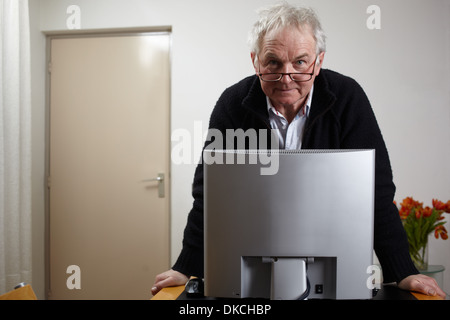 Senior man at home standing in front of personal comuter Stock Photo