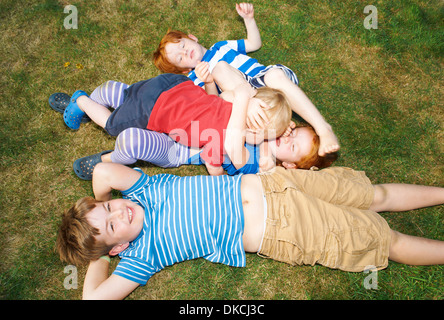 Three brothers and sister lying on grass in garden Stock Photo