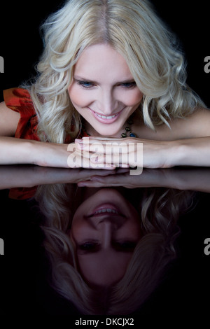 Woman looking at reflection of herself on table Stock Photo