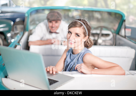 Man watching woman use laptop in back seat of convertible Stock Photo