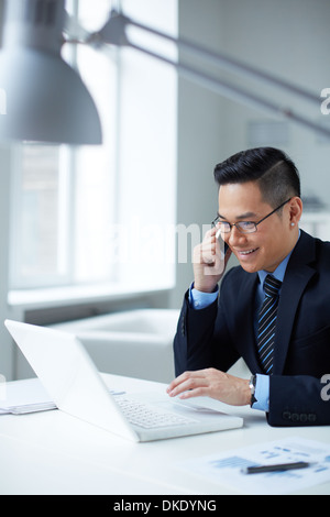 Young businessman in formalwear using laptop and calling in office Stock Photo