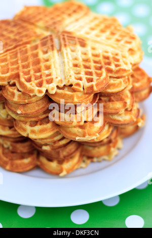 Pile of many waffles on a plate on top of dotted green table cloth Stock Photo
