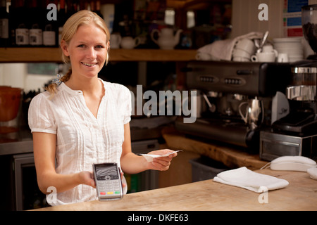 Portrait of young waitress holding credit card reader at kitchen counter