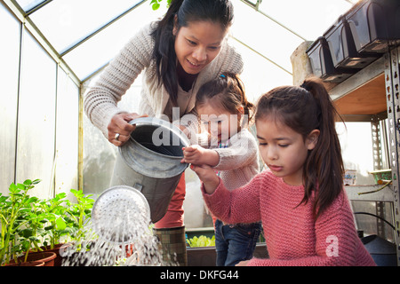 Mother and daughters watering plants in greenhouse Stock Photo