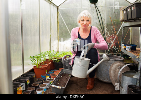 Mature woman holding watering can in greenhouse Stock Photo