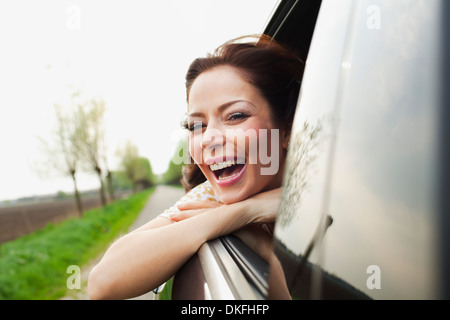 Young woman leaning out of car window, laughing Stock Photo
