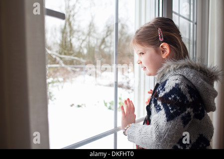 Young girl looking out of window at garden in snow Stock Photo