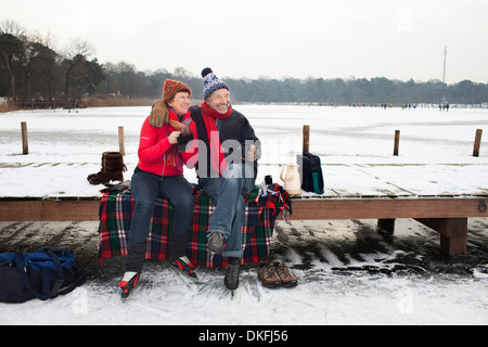 Couple sitting on pier having hot drink Stock Photo